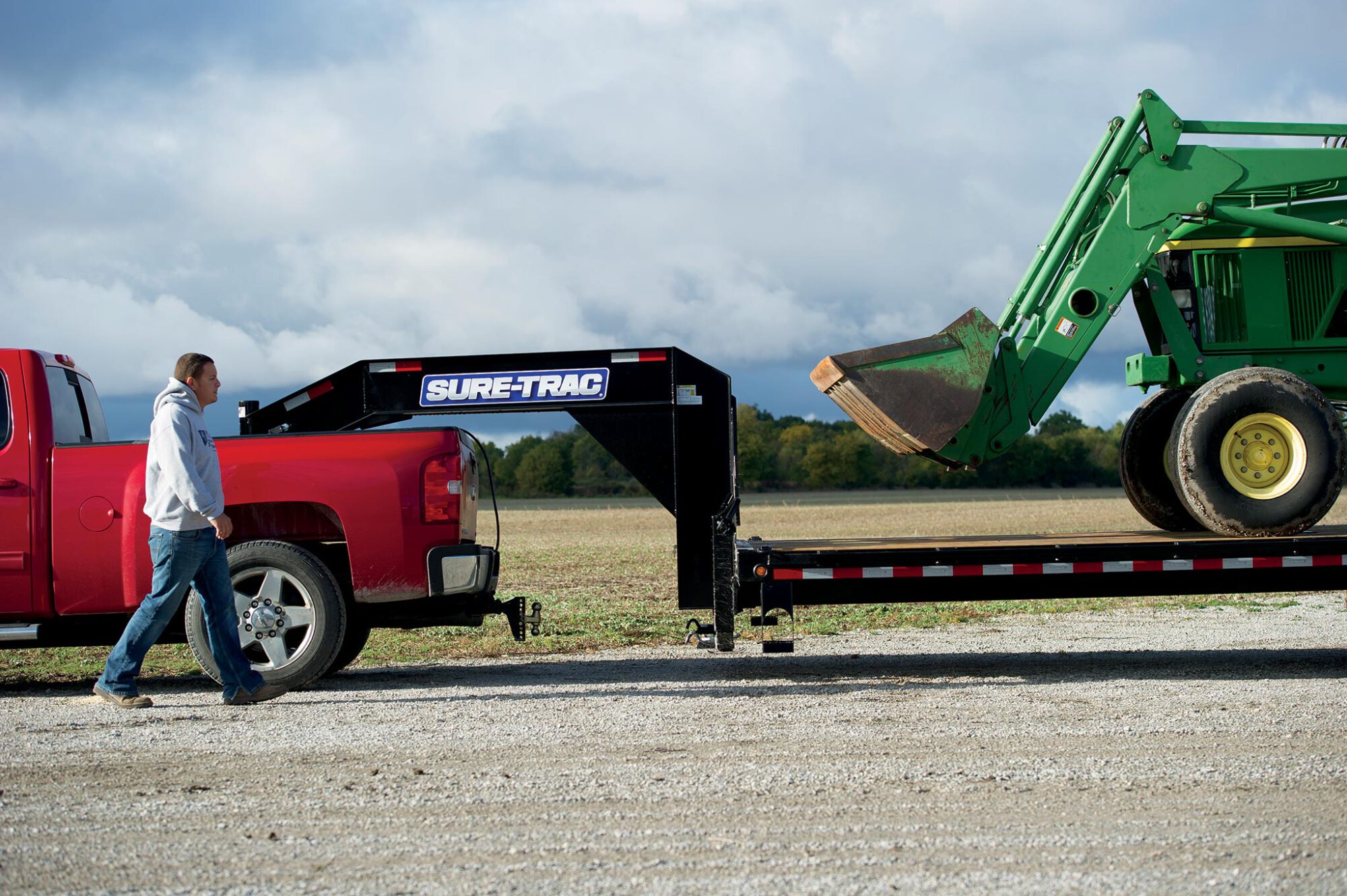 zoomed out sideview ofĀ a tractor being pulled on the heavy duty low profile hydraulic beavertail deckover trailer by a red truck