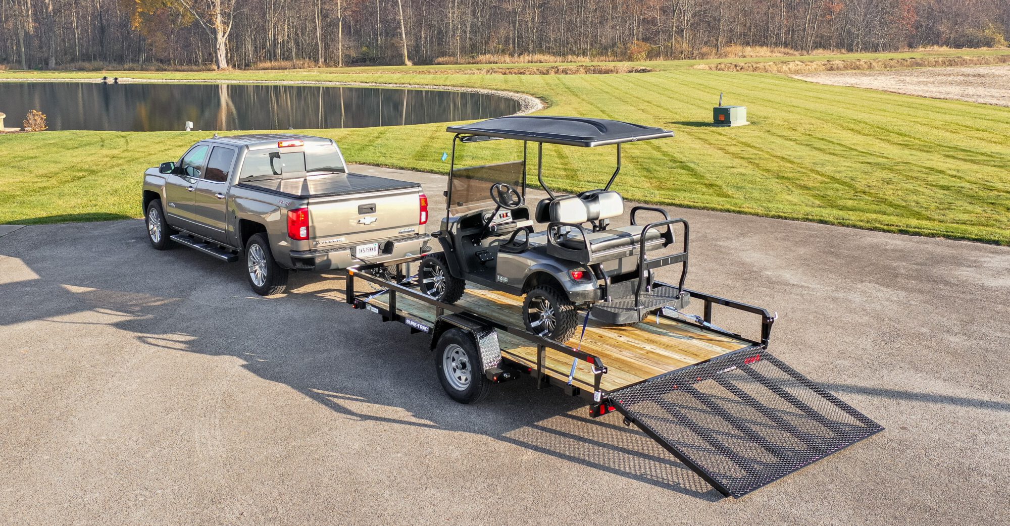 truck pulling a trailer holding a golf cart next to a pond