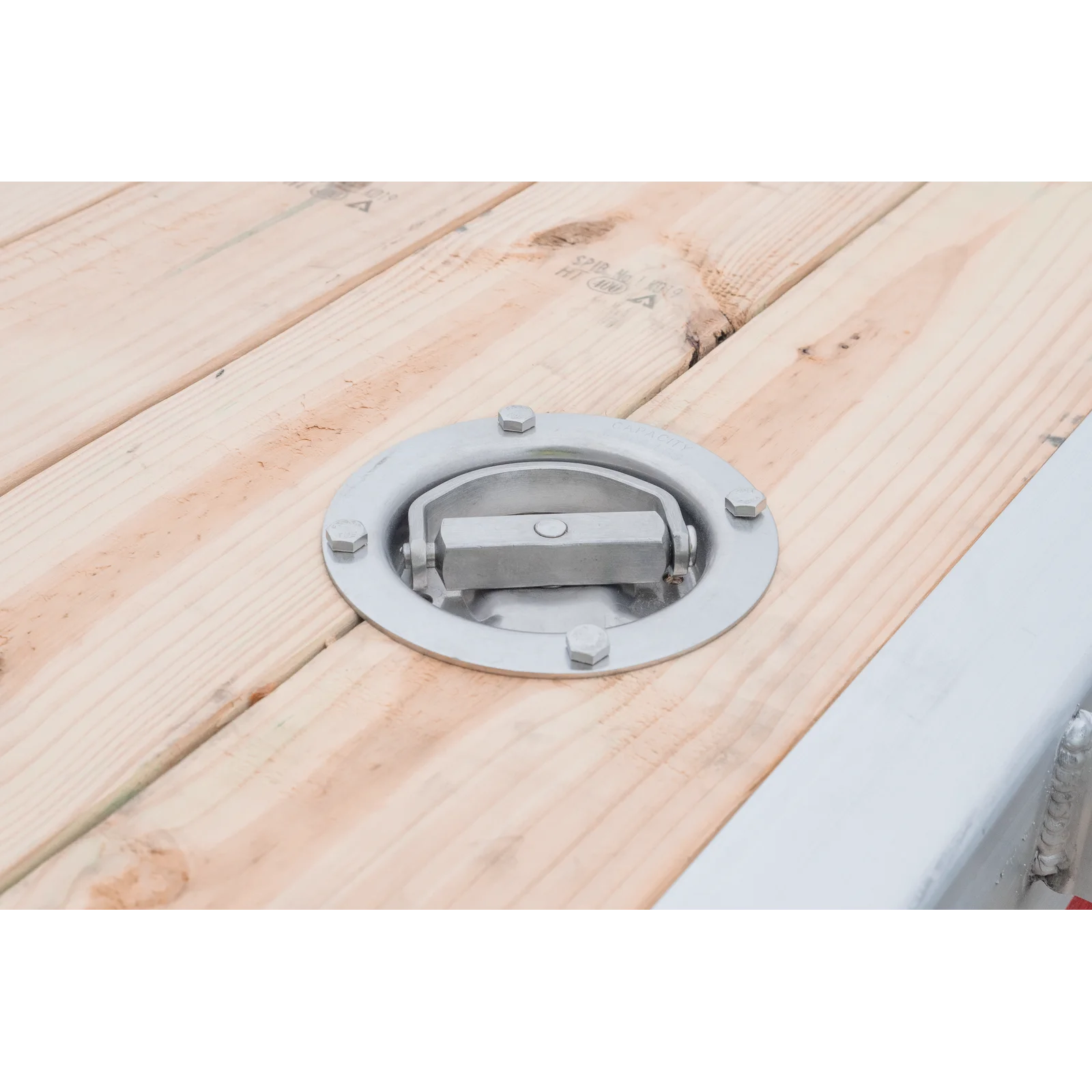 Circular metal deck fastener with a central latch set into light wood planks, likely on a wooden platform or boat deck