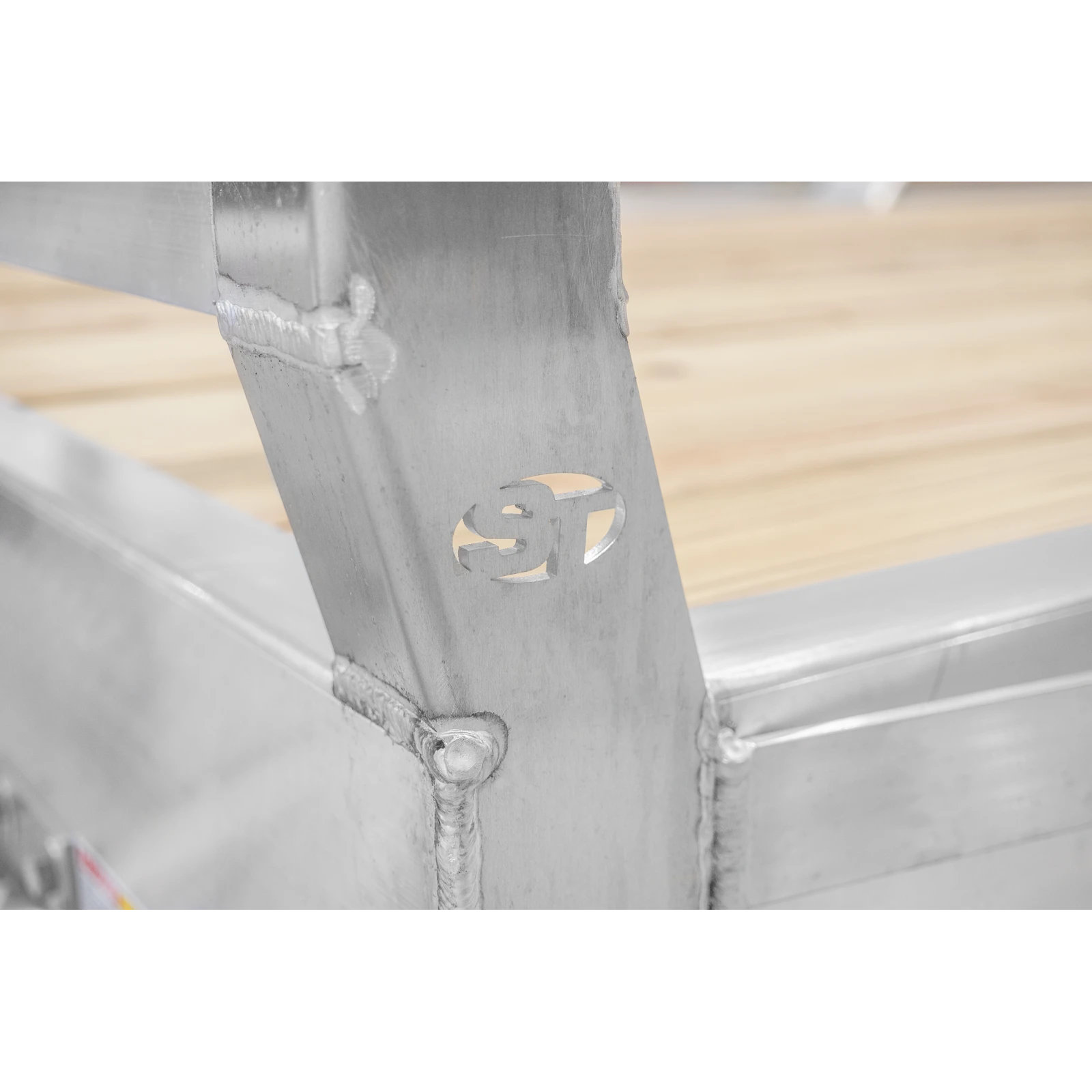Close-up of welded steel frame with a circular cut-out ornament, set against a wooden floor backdrop.