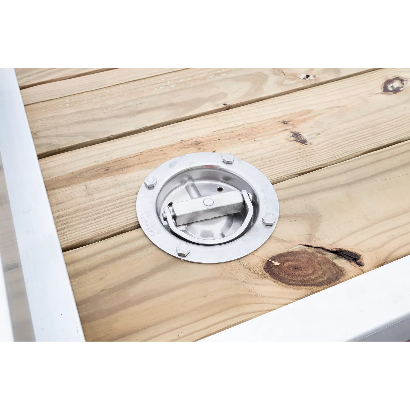 Close-up of a circular metal deck mount bolted to wooden planks, with a central lever-based latch.
