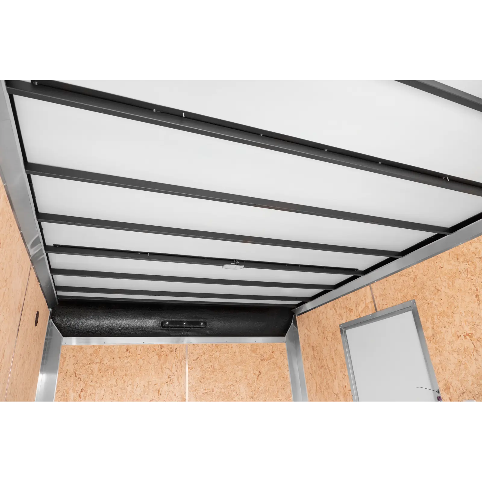 Industrial trailer or elevator interior with white ceiling panels, grey steel beams, and wood-paneled walls; doorway visible on the right