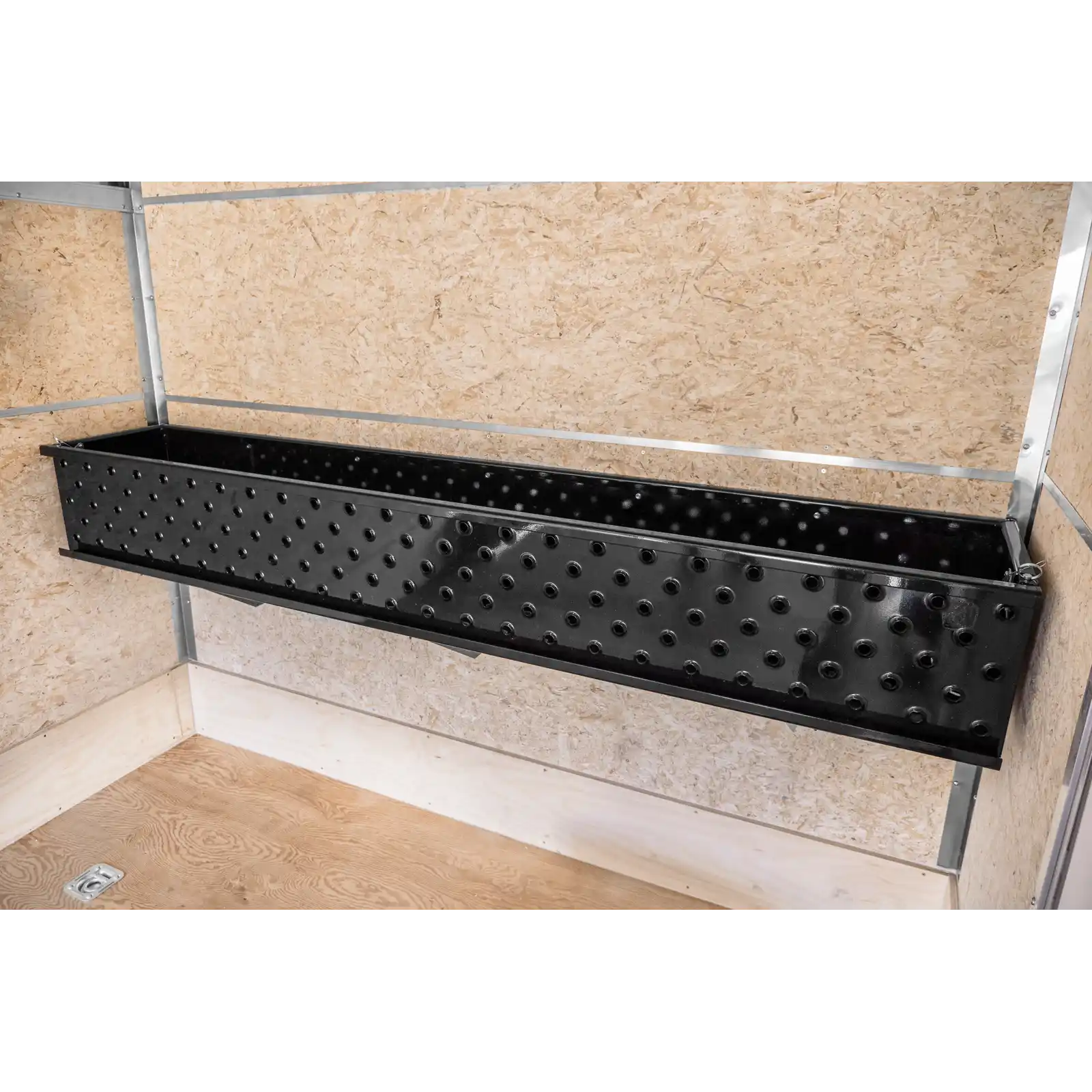 Black perforated metal trough mounted to a wall frame, used for tool storage in a workshop setting