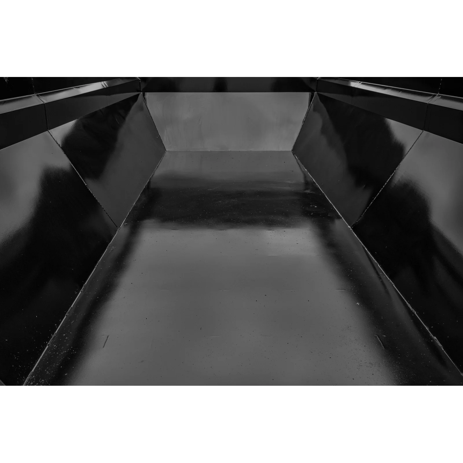 Interior of a glossy, angular metal chute seen from the far end, converging toward the opening in a monochrome scene
