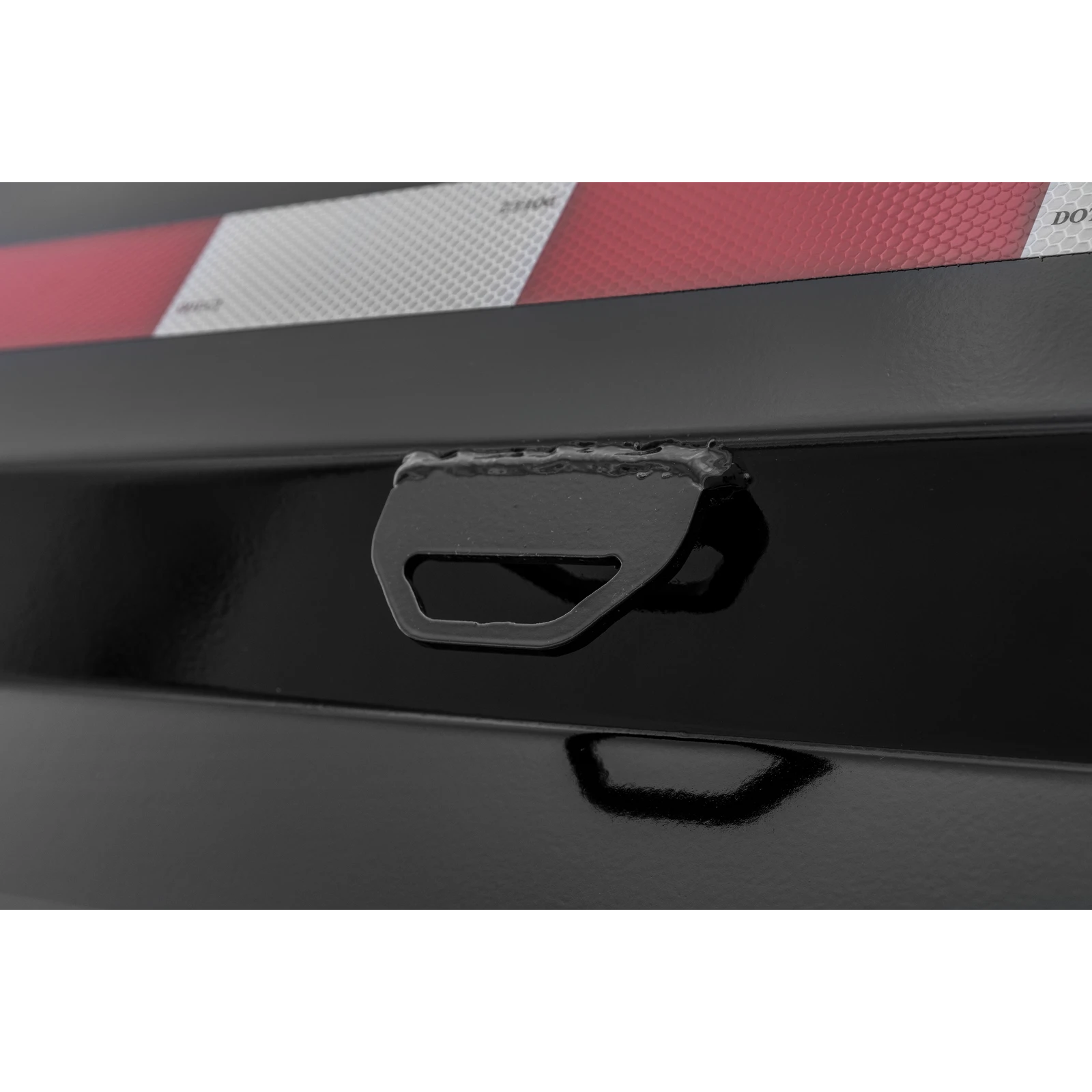 Close-up of a black trailer frame with a metal latch and a red-and-white reflective strap