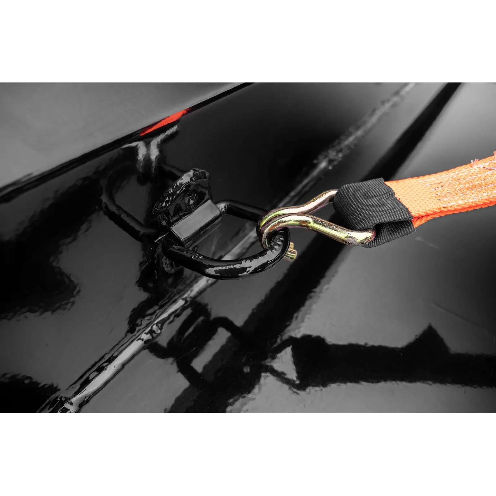 Close-up of an orange strap with a metal hook clipped to a glossy black surface, showing reflections in the shine.