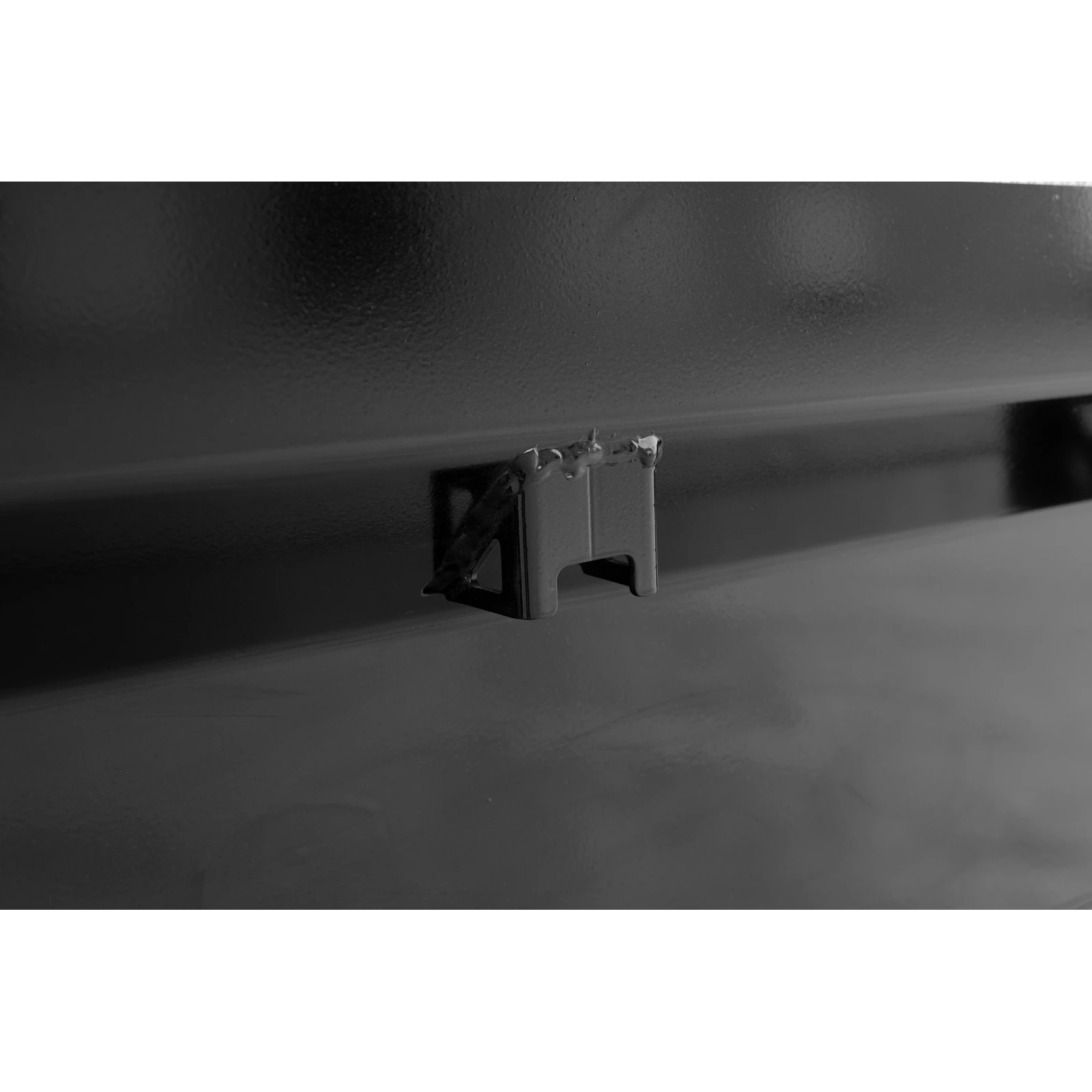 Close-up of a small metal latch attached to a dark, glossy surface in a monochrome photo.
