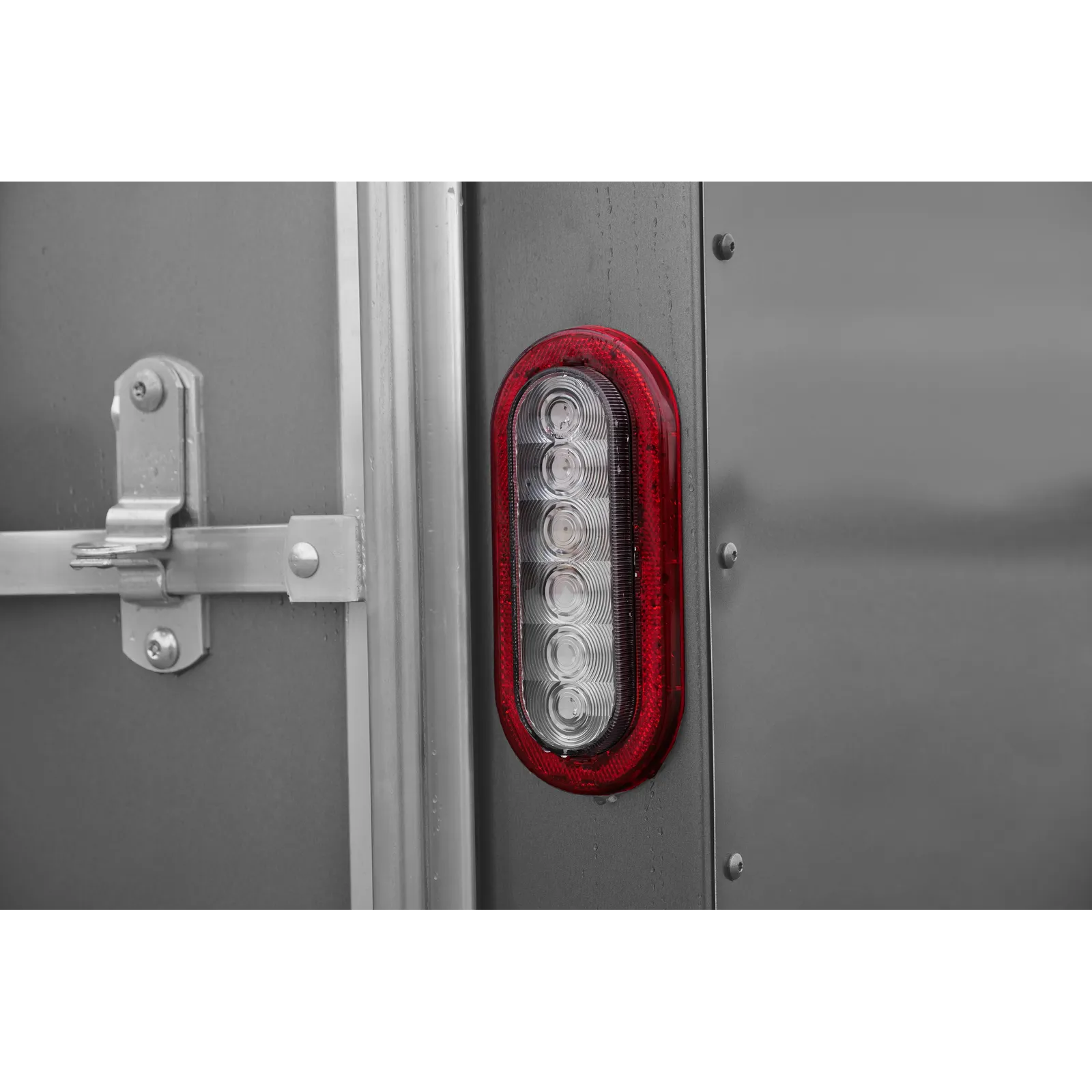 Rear red tail light on a gray metal trailer, with a latch and hinge visible to the left