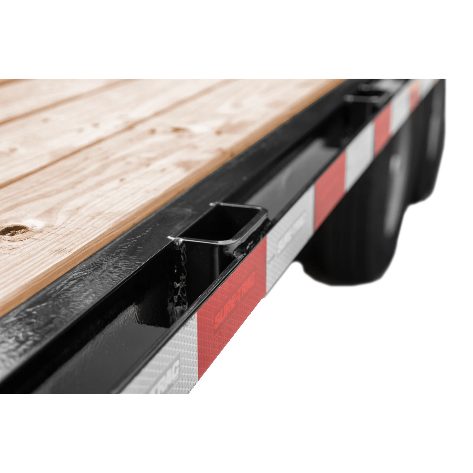 Close-up of a wooden deck on a black metal trailer with red-and-white hazard stripes along the side.