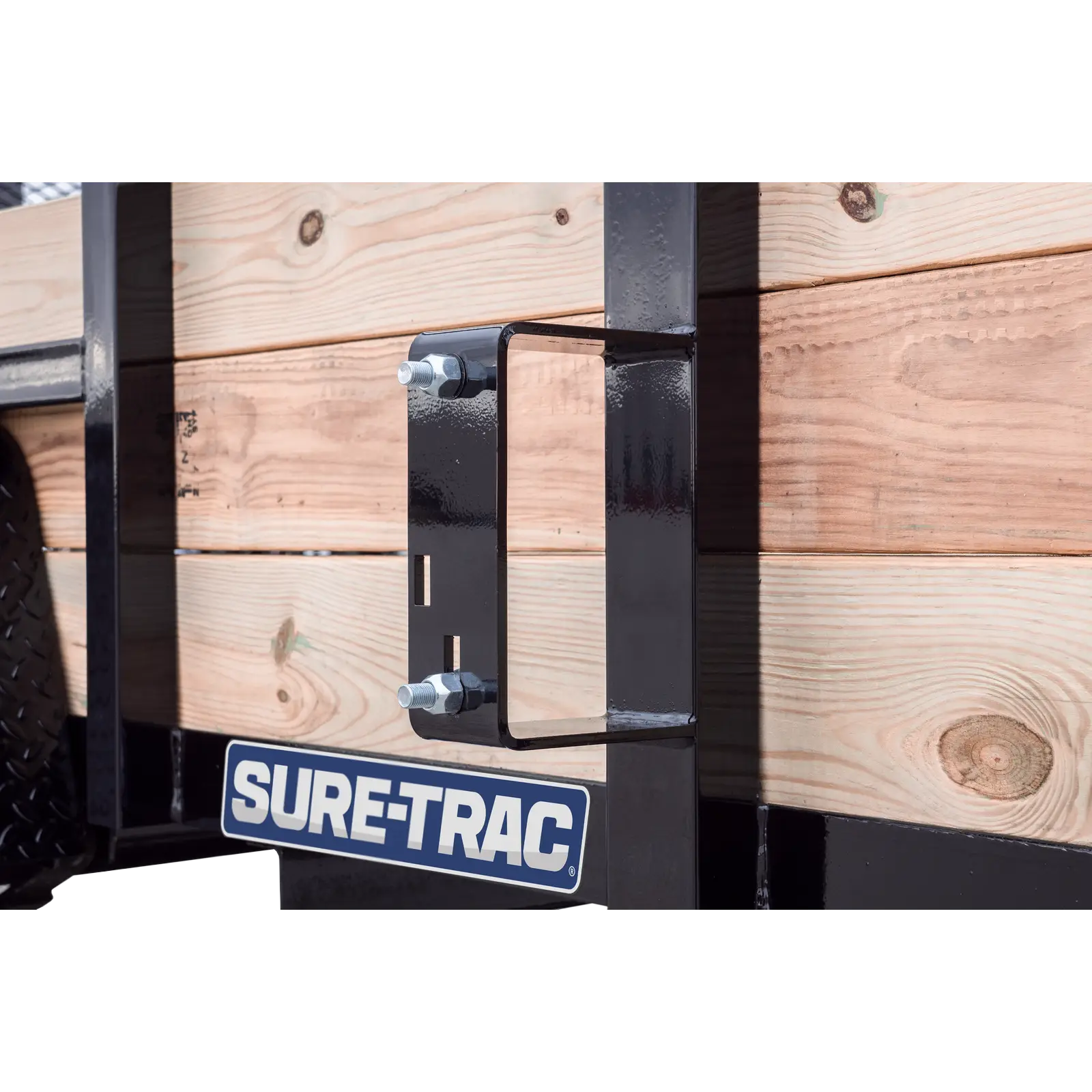 Close-up of a black metal mounting bracket bolted to a wooden trailer bed with a Sure-Trac logo plate visible underneath.